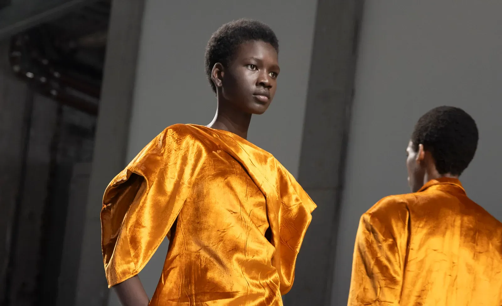 A model wearing a lustrous metallic orange dress with structured shoulders walks confidently on the runway, embodying the essence of Dawei's Fall/Winter 24/25 collection, which merges classic elegance with a modern edge.