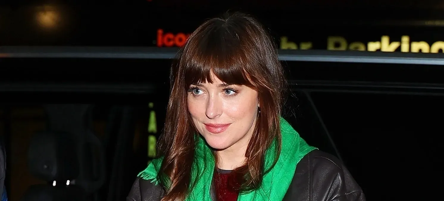 Dakota Johnson holding a black Bottega Veneta bag, wearing a green scarf and leather coat in NYC.