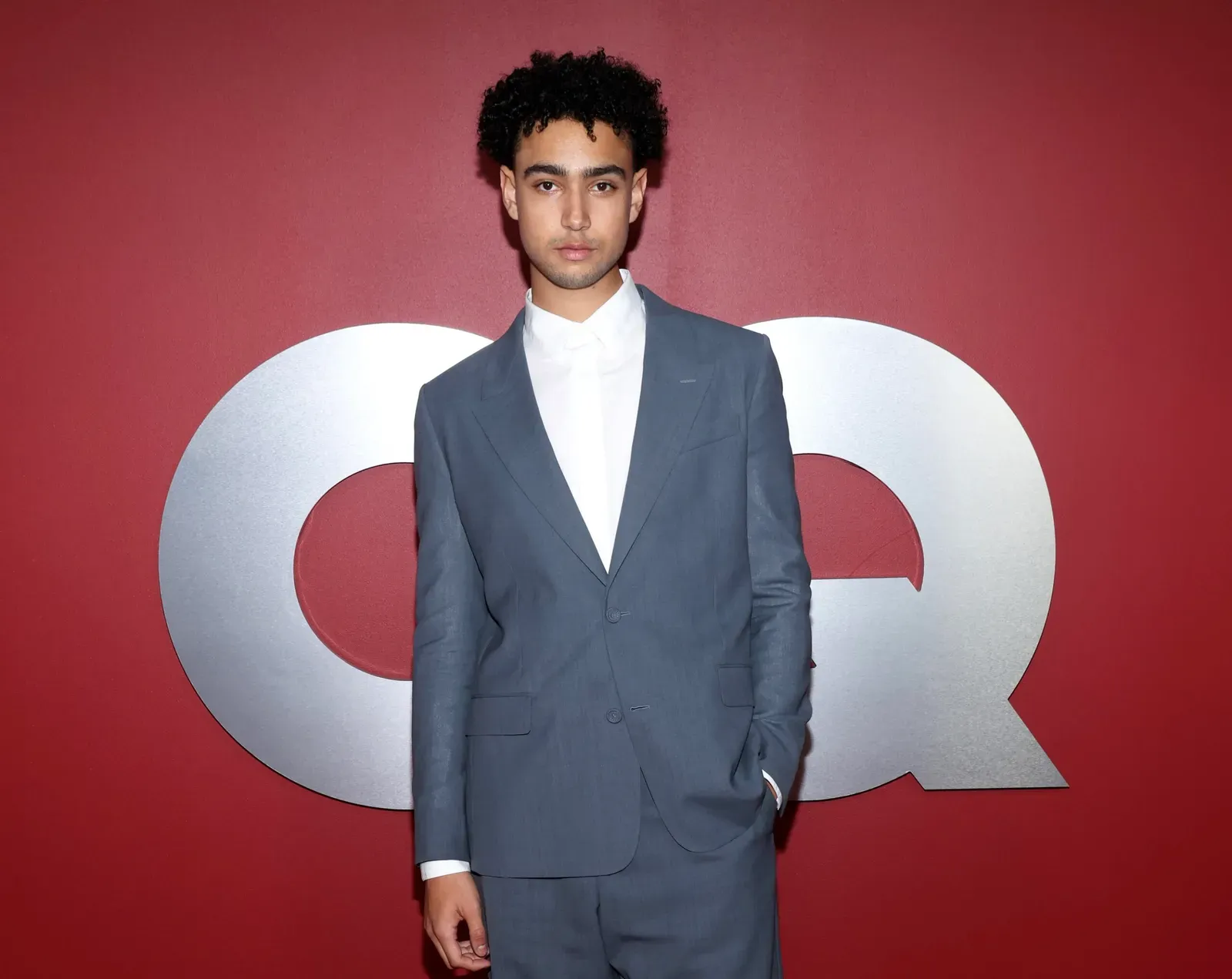 Archie Madekwe stands confidently at the GQ Men of the Year Party 2023 in Los Angeles, clad in a tailored grey suit and white shirt, embodying the essence of modern sophistication.
