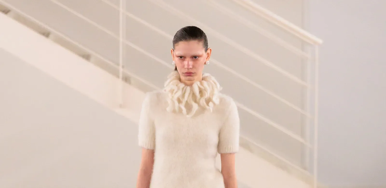 A model presents Look 10 from SUNNEI's Fall/Winter 2024 collection at Milan Fashion Week, wearing an oversized blue mohair sweater and skirt with red footwear and a yellow accessory.
