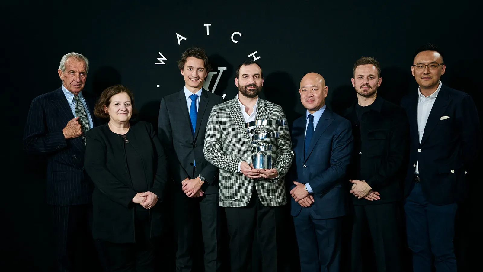 A group of individuals posing together at an event, with one man holding a spiral-shaped silver trophy.
