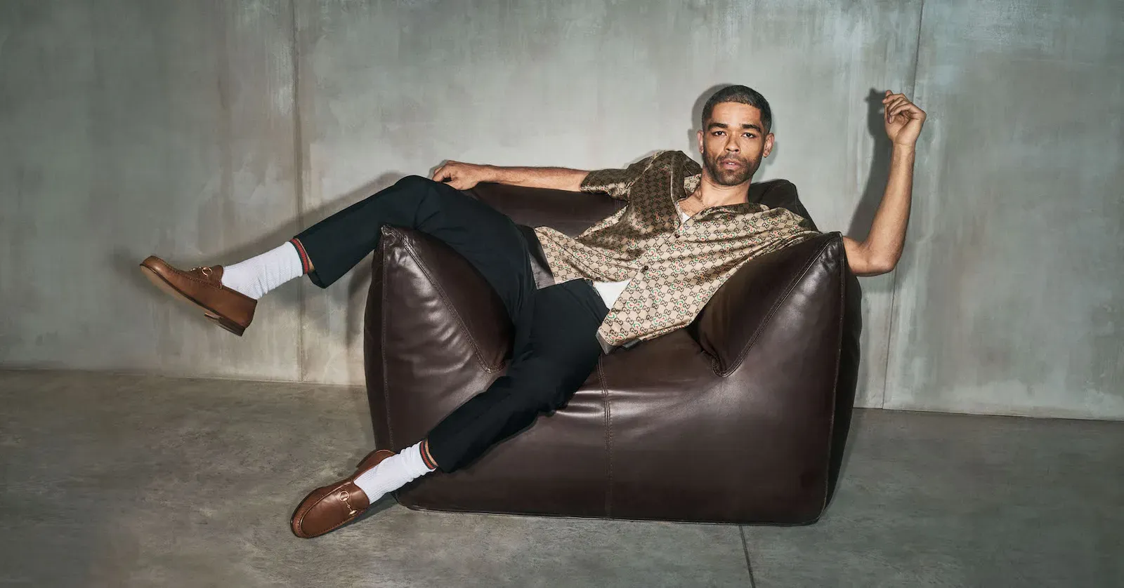 Kingsley Ben-Adir lounges effortlessly in Gucci's reimagined Horsebit 1953 loafer, showcasing relaxed sophistication.