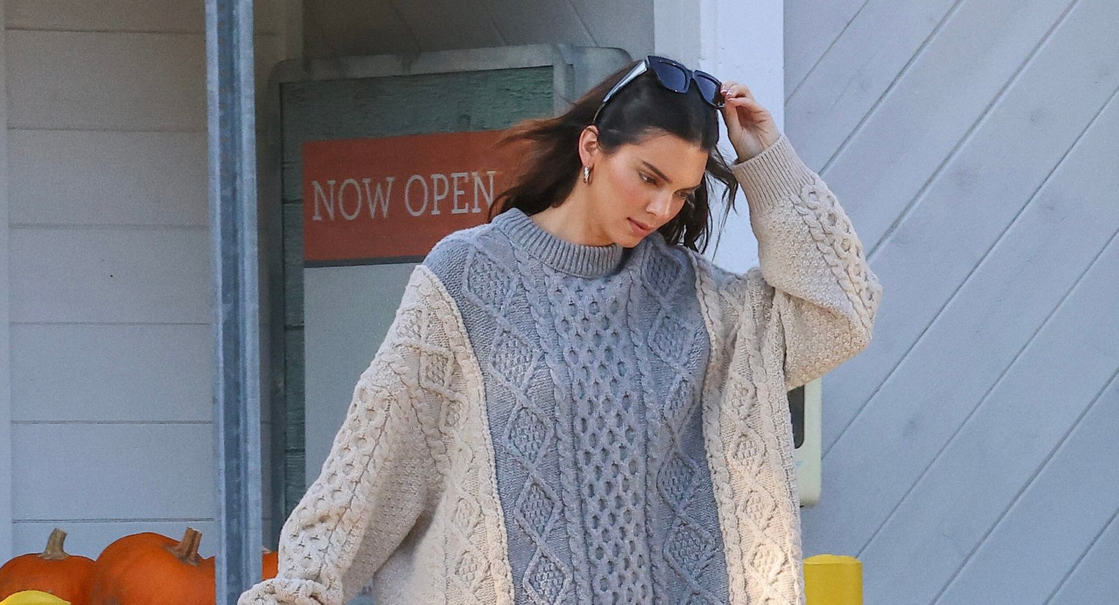 Kendall Jenner stepping out in a chunky knit sweater by Bottega Veneta, carrying a large tote and a bouquet of sunflowers, showcasing a relaxed yet luxurious style.