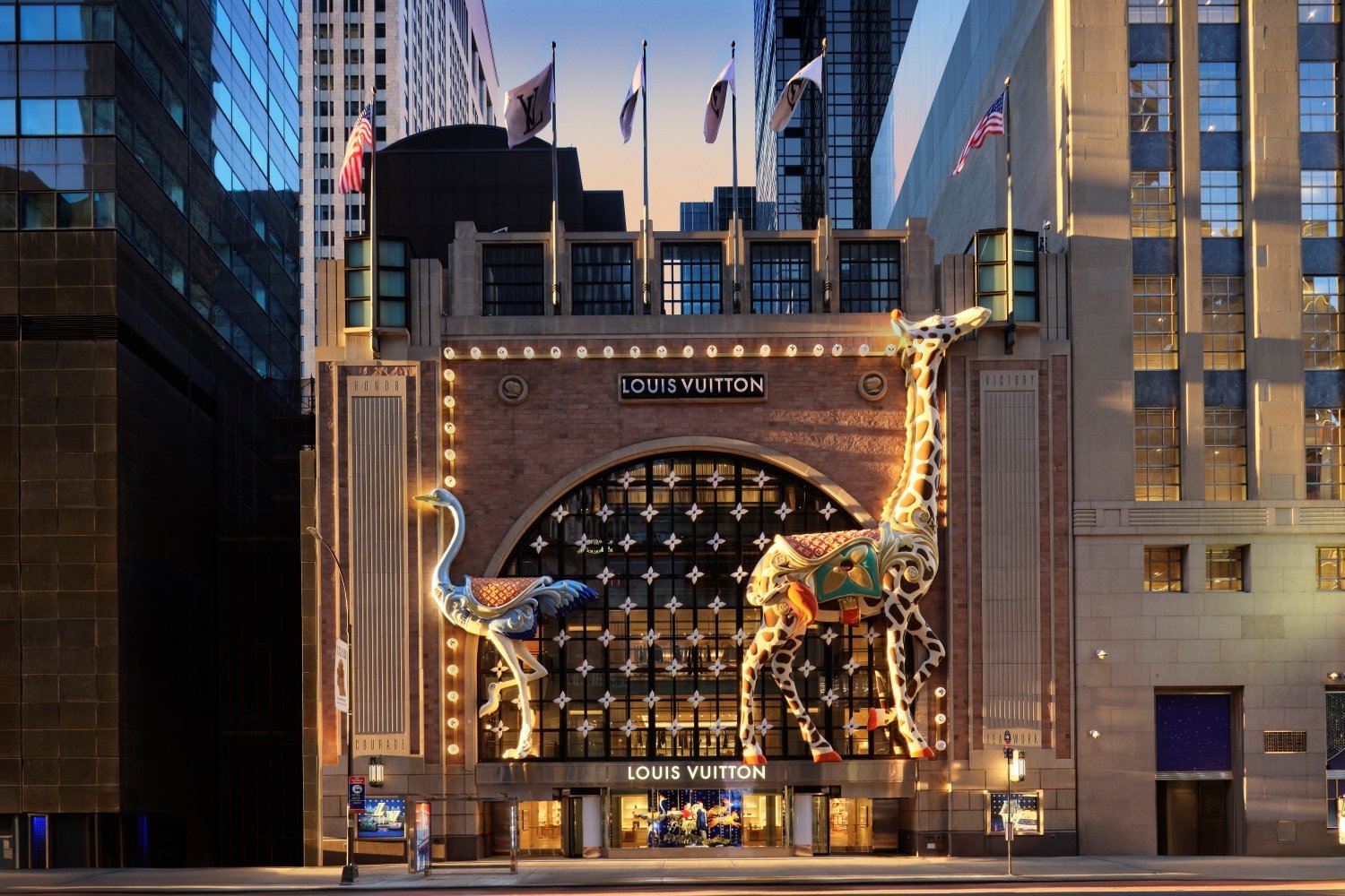 The temporary flagship’s Art Deco façade is brought to life with a whimsical carousel-themed holiday installation, featuring oversized illuminated giraffe and ostrich figures that frame the grand archway entrance.
