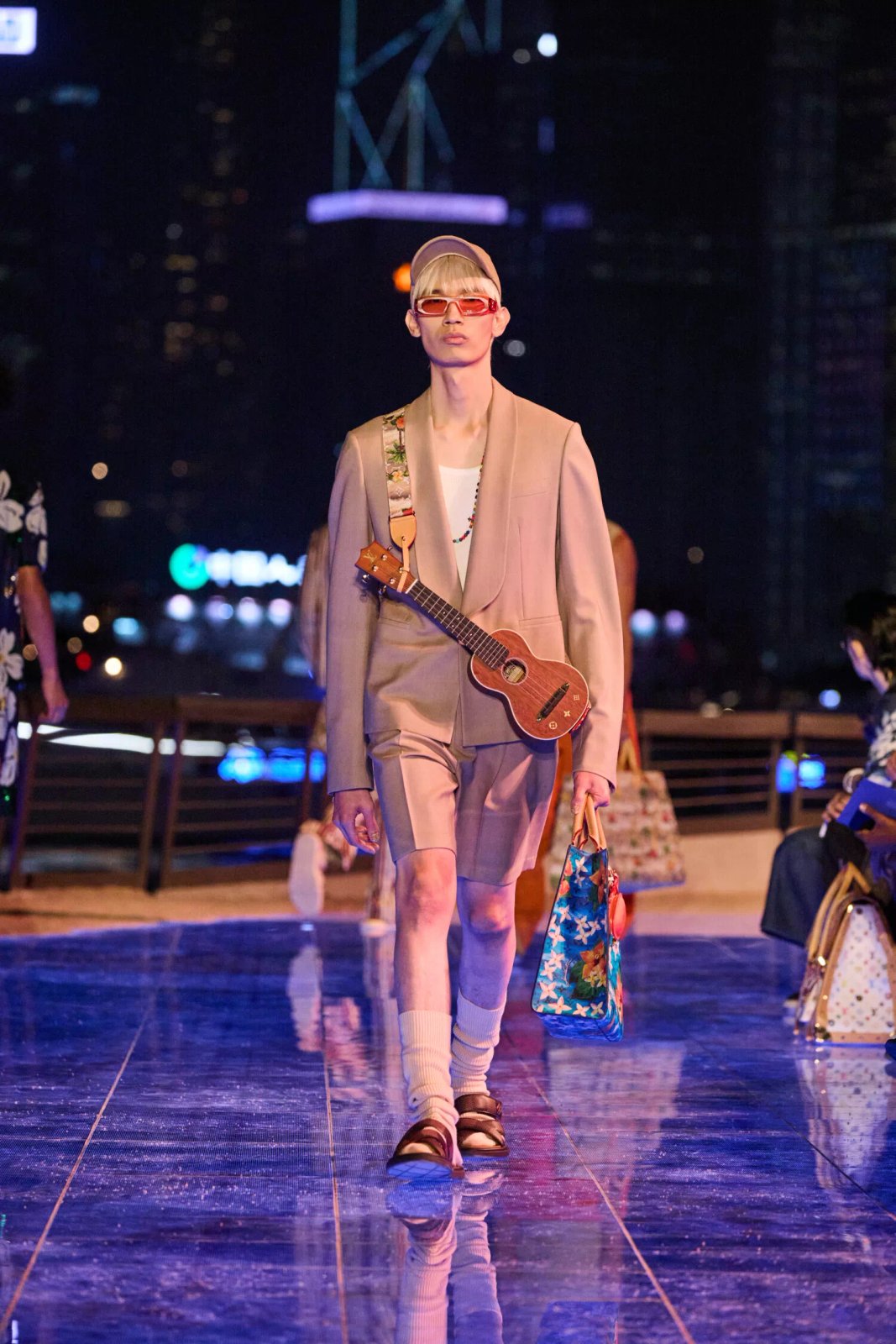 A model channels the spirit of travel with a ukulele and a splash of tropical prints, representing the Louis Vuitton Men’s Pre-Fall 2024 collection’s theme of global exploration.