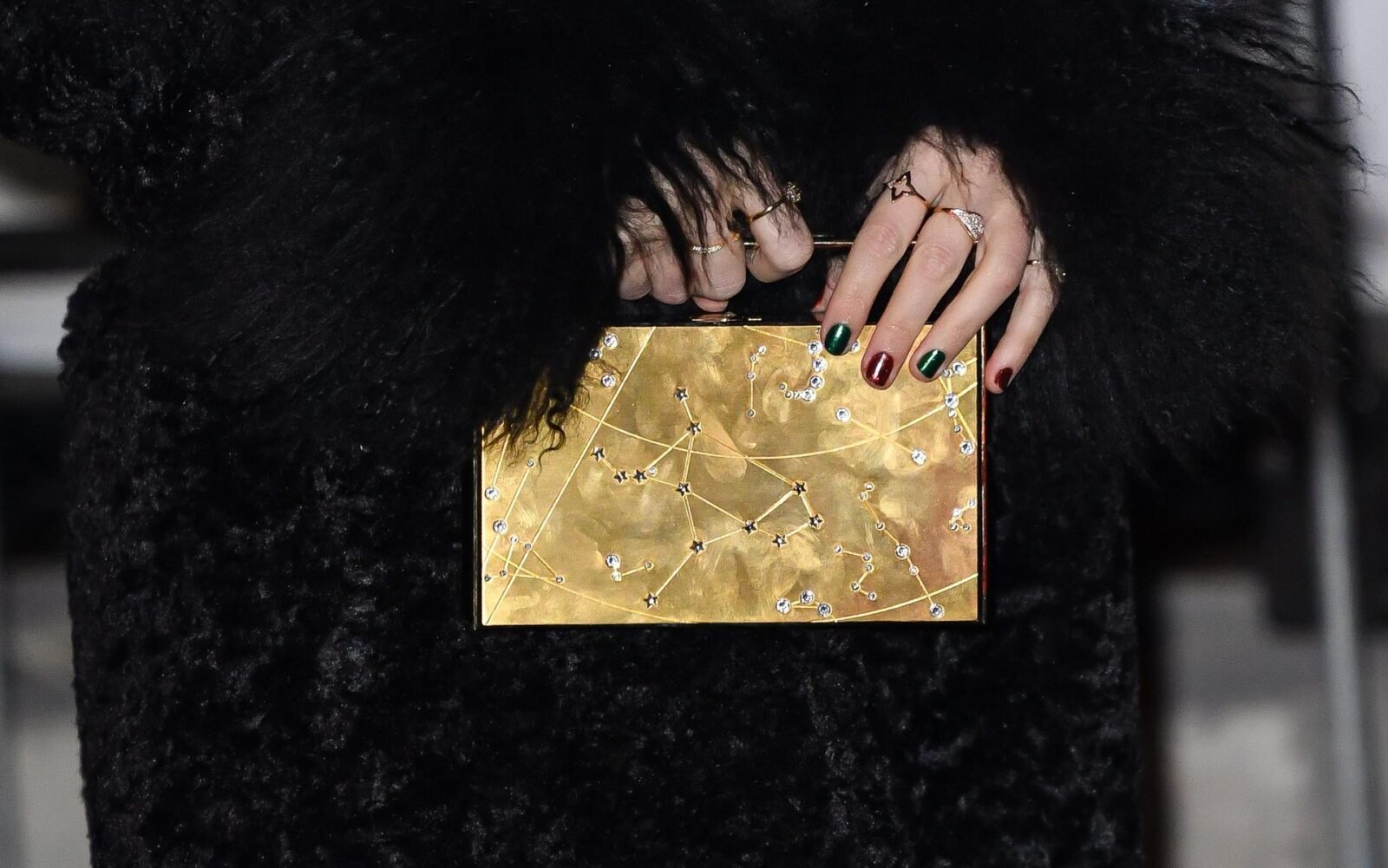 Taylor Swift's elegant grasp in the Louis Vuitton Blossom Jewelry Collection—complements her chic ensemble and astrological inspired clutch, showcasing her keen eye for accessorizing with sophistication. Image courtesy of Louis Vuitton.