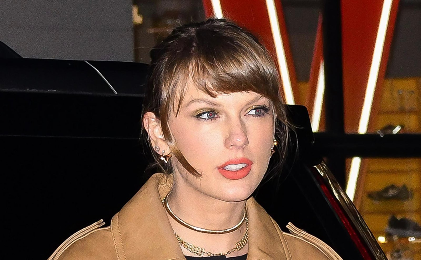 Taylor Swift in Manhattan wearing a classic trench coat paired with Louis Vuitton Blossom Fine Jewelry, exuding luxurious style in a metropolitan setting.
