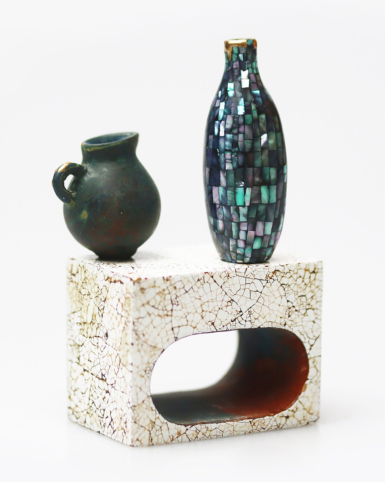 Two ceramic vases of contrasting sizes and textures on a cracked white pedestal with a hollow center.