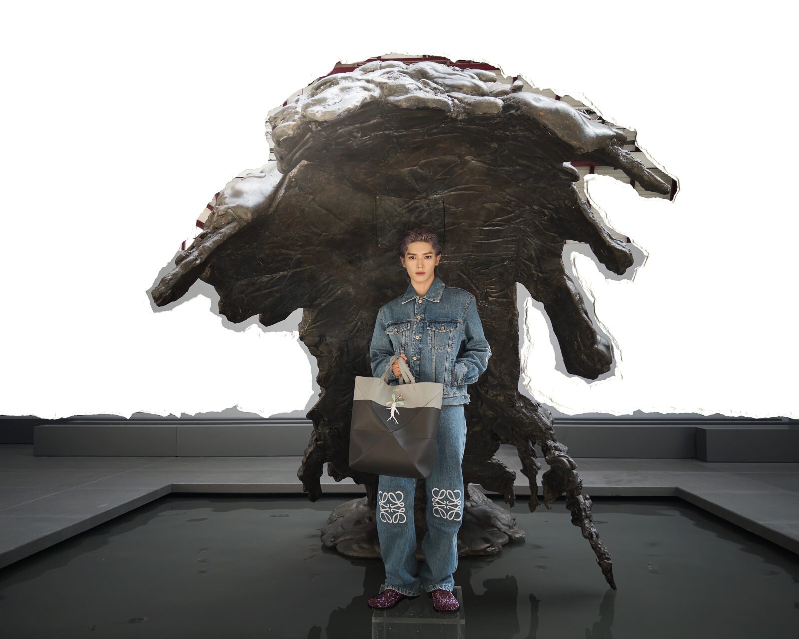 TAEYONG drips in denim with a LOEWE tote in hand beneath an artistic sculpture.