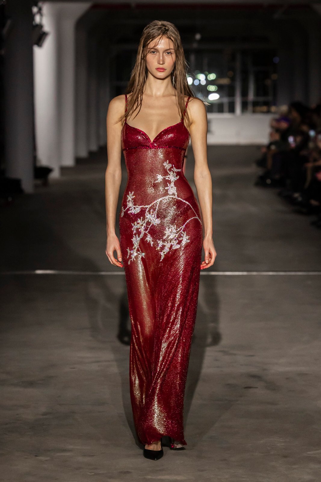A model gracefully showcases a sparkling red sequined gown with delicate white floral accents, featuring a deep neckline and fitted silhouette, at Ludovic de Saint Sernin