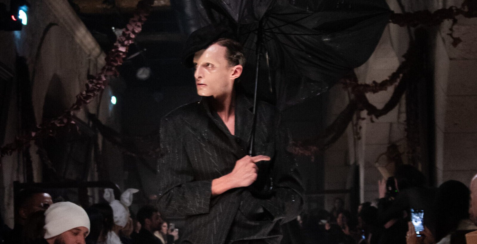 A model from Maison Margiela's Artisanal 2024 collection strikes a pose with a dramatic oversized umbrella on the runway.