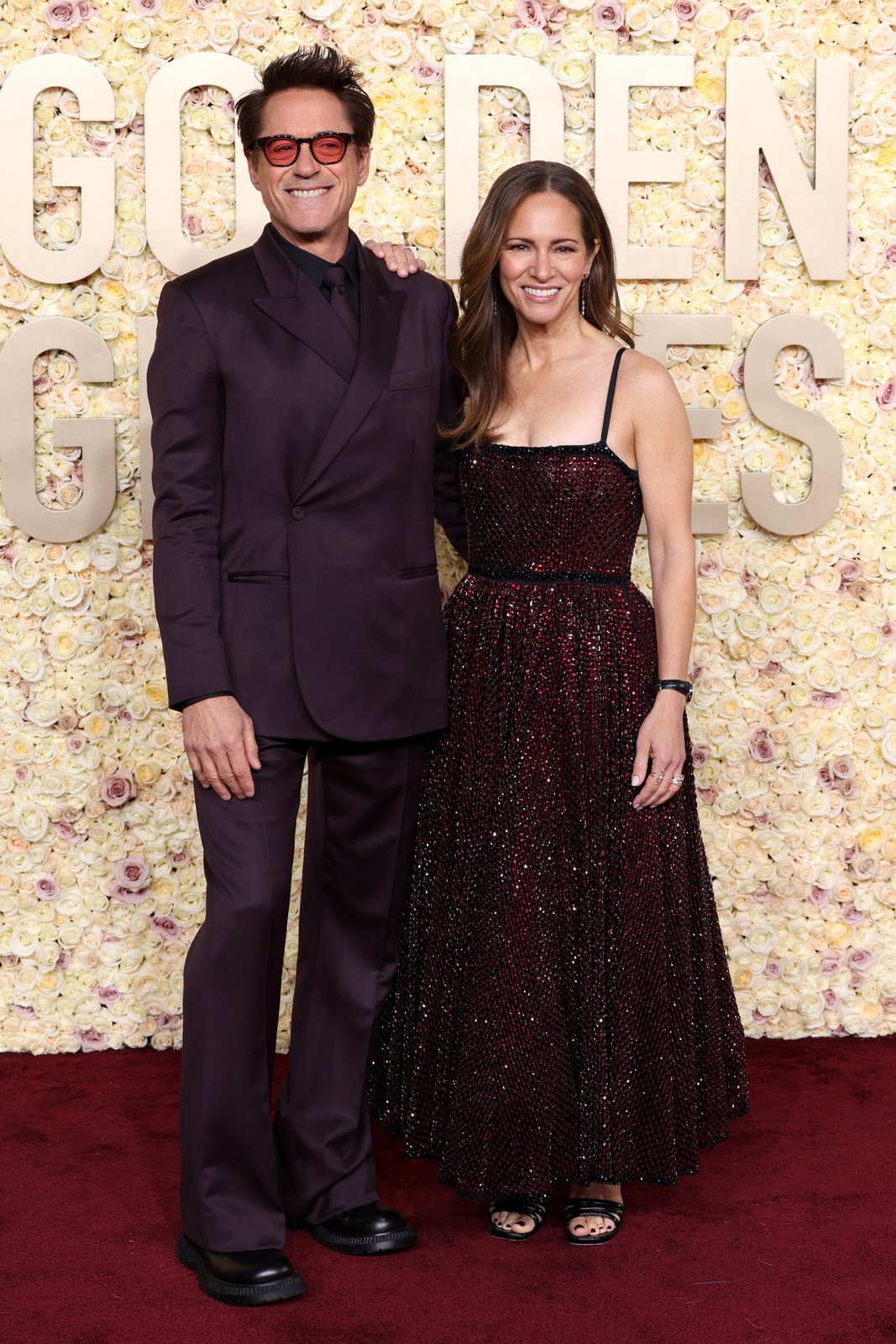 Robert Downey Jr. and Susan Downey strike a harmonious pose, with Downey in a Dior Men's burgundy wool and silk oblique suit, black shirt, and burgundy silk tie, complemented by his wife's sparkling elegance. (Photo by Kevin Mazur/Getty Images)
