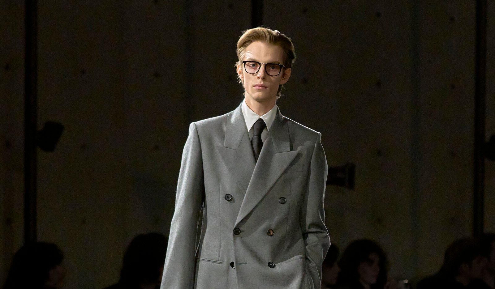 Leon Dame walks down the runway at Saint Laurent's Winter 2024 menswear show, wearing a double-breasted, loose-fitting light grey suit with resolute peak lapels, embodying a modern twist on 1980s power dressing.