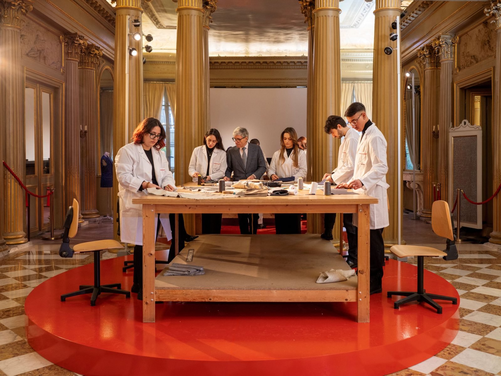 Students from Kiton's Scuola di Alta Sartoria showcase traditional tailoring techniques within the ornate halls of the Istituto Italiano di Cultura di Parigi. (Photo: Courtesy of Kiton)