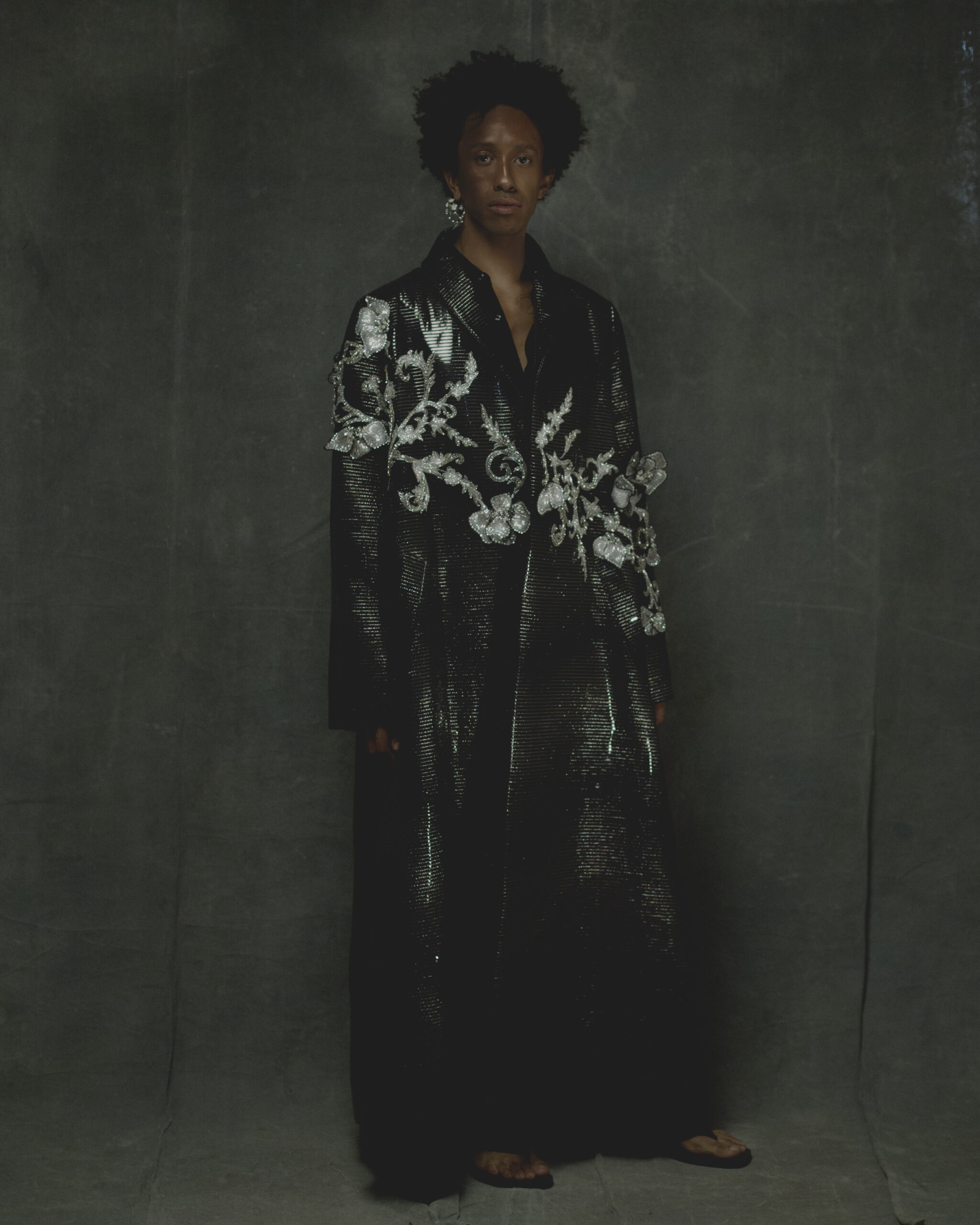 Coat by GEORGES HOBEIKA, shirt and trousers by GCDS, earring by SHAUN LEANE, sandals by HERMÈS
