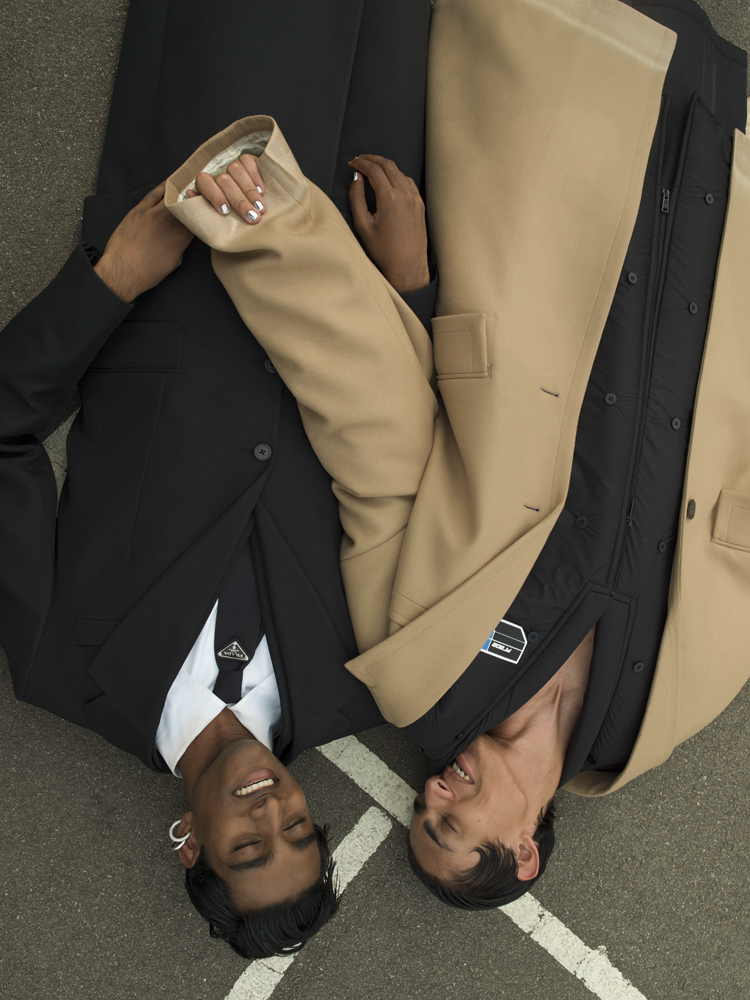 Jeenu wears coat, suit, shirt, and tie by PRADA, earring by ALAN CROCETTI. Benjamin wears coats by PRADA