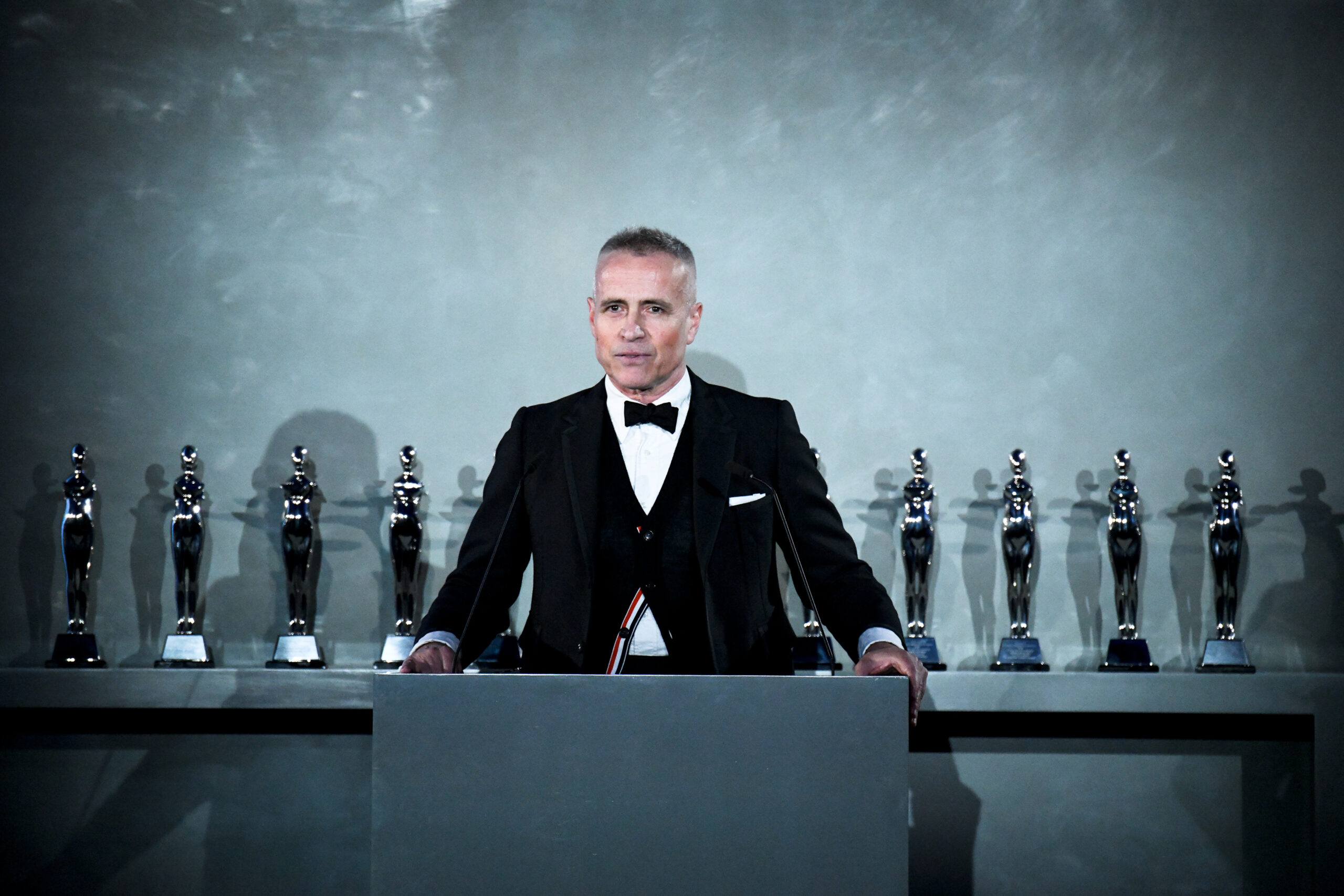CFDA Chairman Thom Browne stands ready at the podium, with the evening's coveted awards lined up behind him, set to celebrate the industry's top talents at the prestigious CFDA Fashion Awards presented by Amazon. CFDA Chairman Thom Browne stands ready at the podium, with the evening