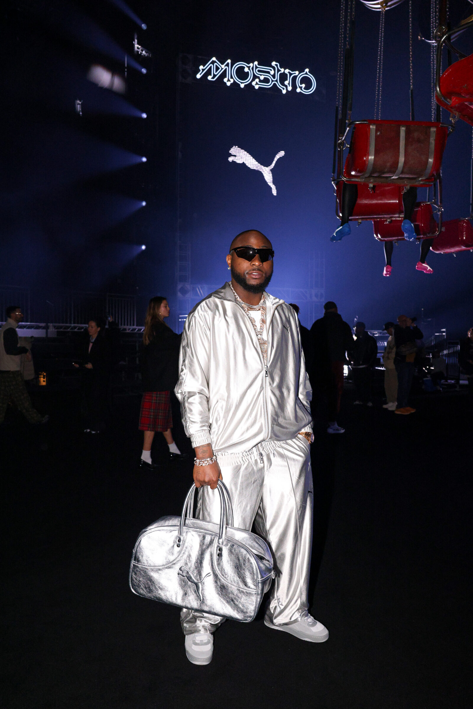 Davido exudes confidence at the Puma event, his style a perfect blend of luxury and sport, donning a metallic silver tracksuit complemented by crisp white sneakers and accessorized with a statement Puma duffle bag.