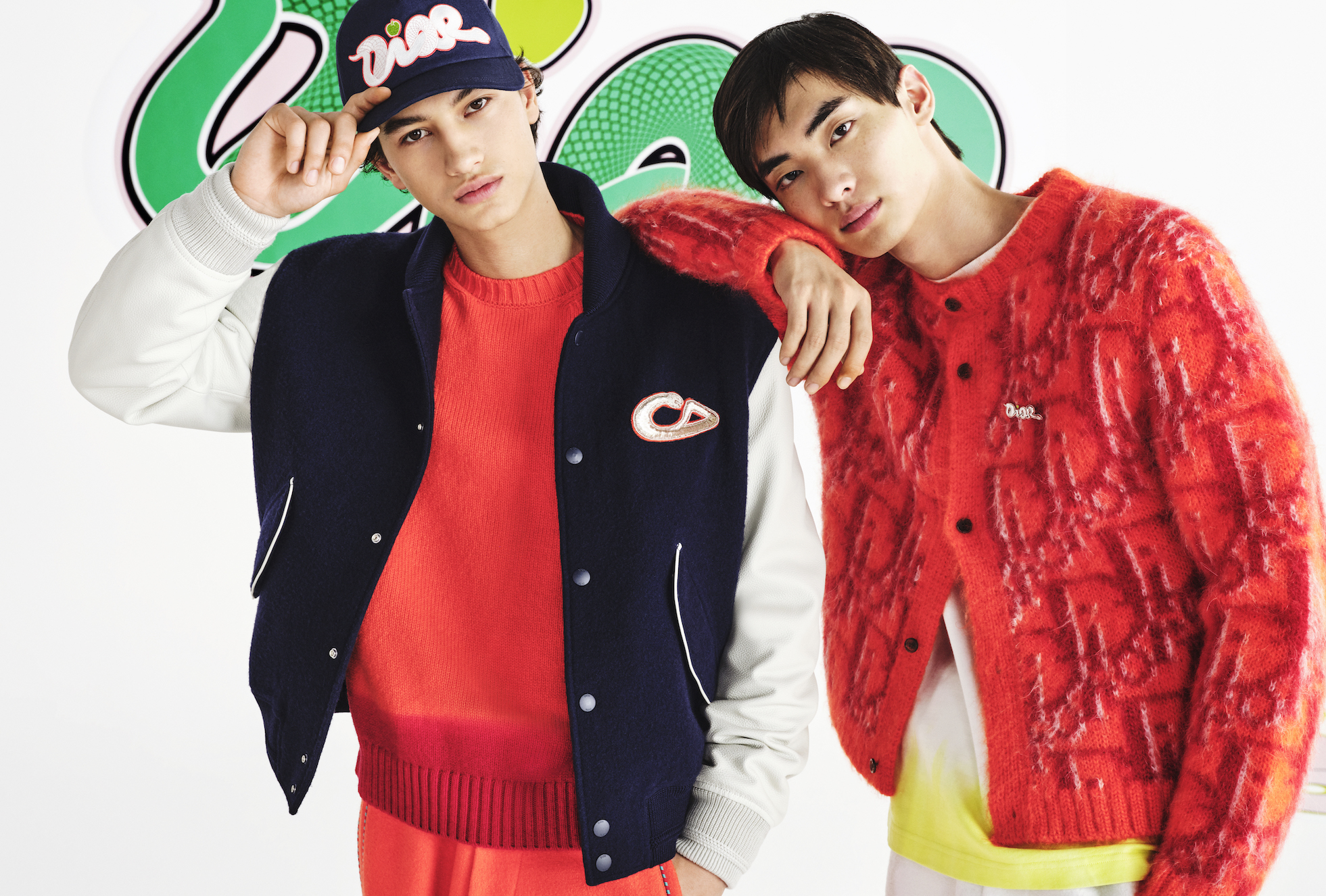 Sporting elements merge with luxury: the varsity jacket finds harmony with a vibrant Mohair and Wool Oblique cardigan against KAWS's dynamic backdrop. (Image: Courtesy of Dior)