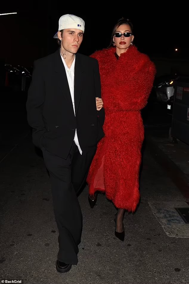 Hailey Bieber exemplifies holiday glamour in a red Ferragamo mini dress and shearling coat, styled by Dani Michelle for the Rhode Holiday Party in Los Angeles. Image courtesy of BackGrid/Ferragamo.