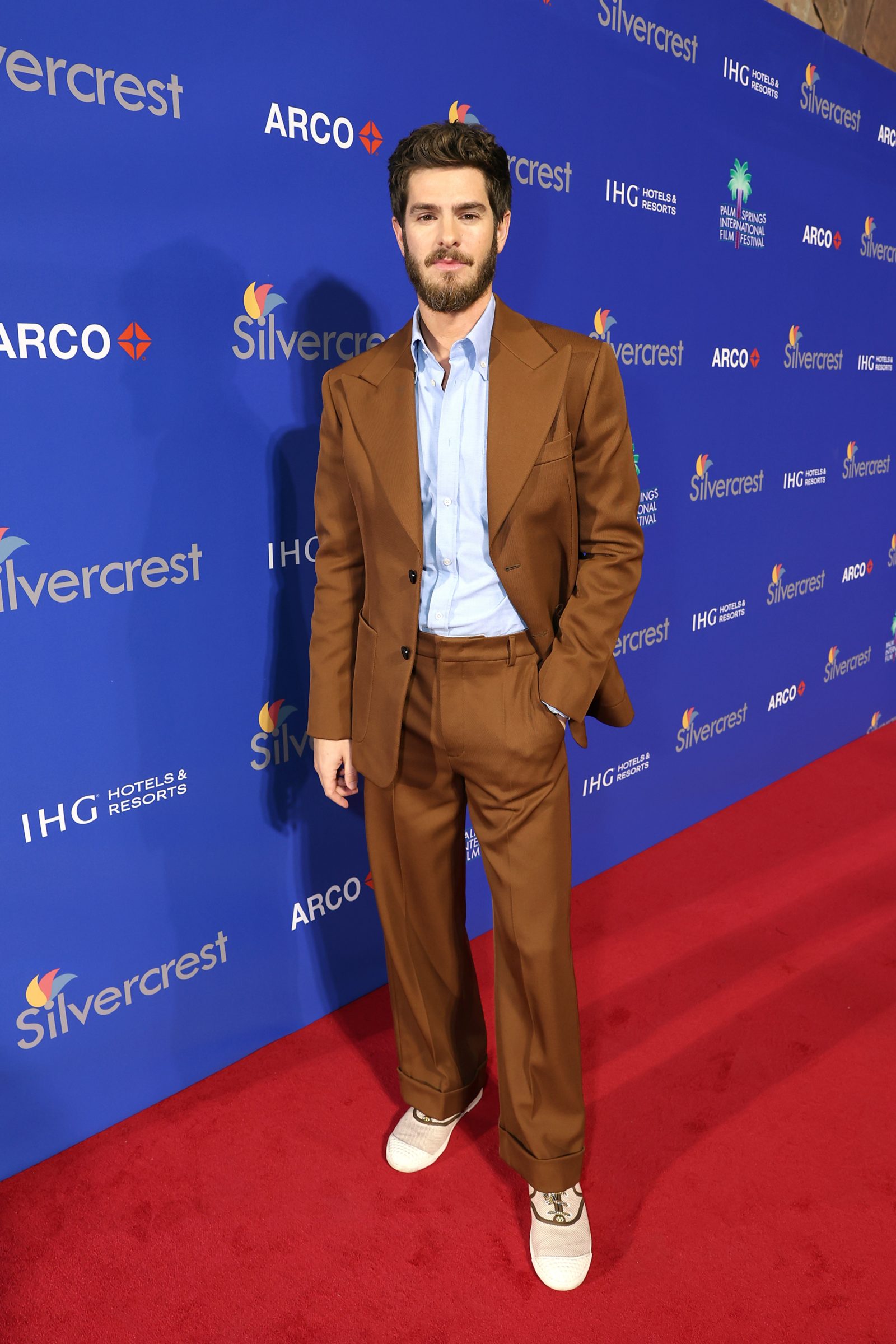 Andrew Garfield arrives at the 36th Annual Palm Springs International Film Festival wearing a custom cognac-colored suit paired with cream leather sneakers, against the Silvercrest and ARCO step-and-repeat. (Photo: Getty Images)