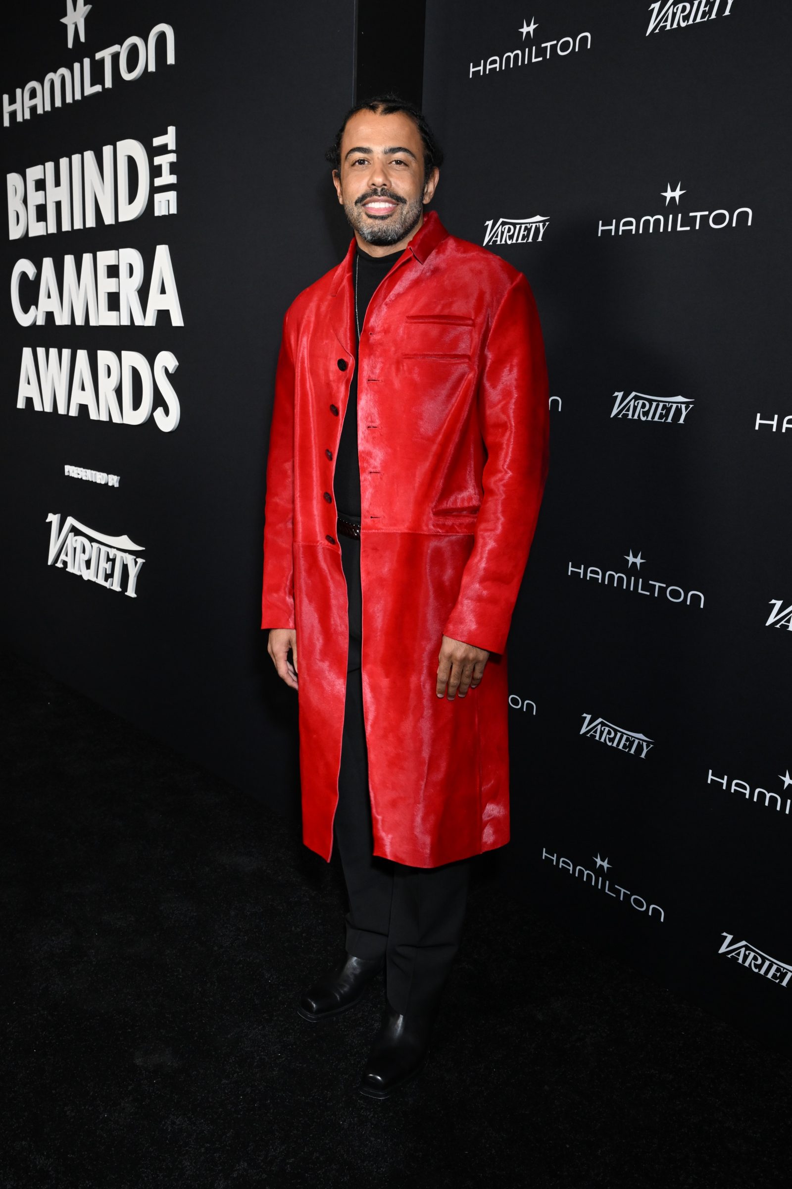 Daveed Diggs makes a bold statement in a scarlet calf hair leather coat from Versace’s Fall-Winter 2024 collection, paired with a sleek black turtleneck and tailored trousers. (Photo: Courtesy of Versace)