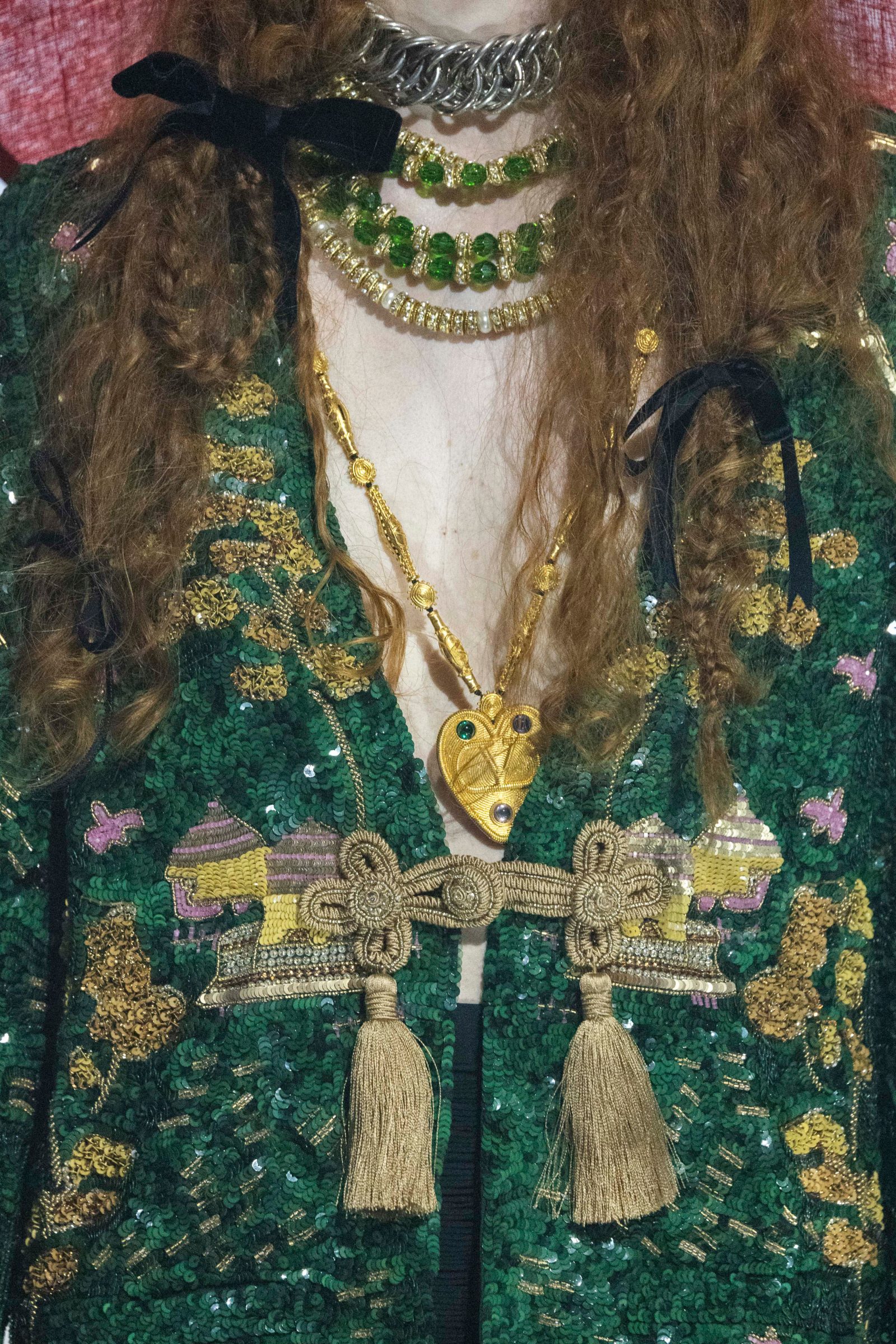 A detail portrait of Byzantine opulence: emerald sequins and metallic embroidery adorn a collared jacket with gilded tassels, while layered crystal necklaces and a heart-shaped pendant complete the ornate composition.