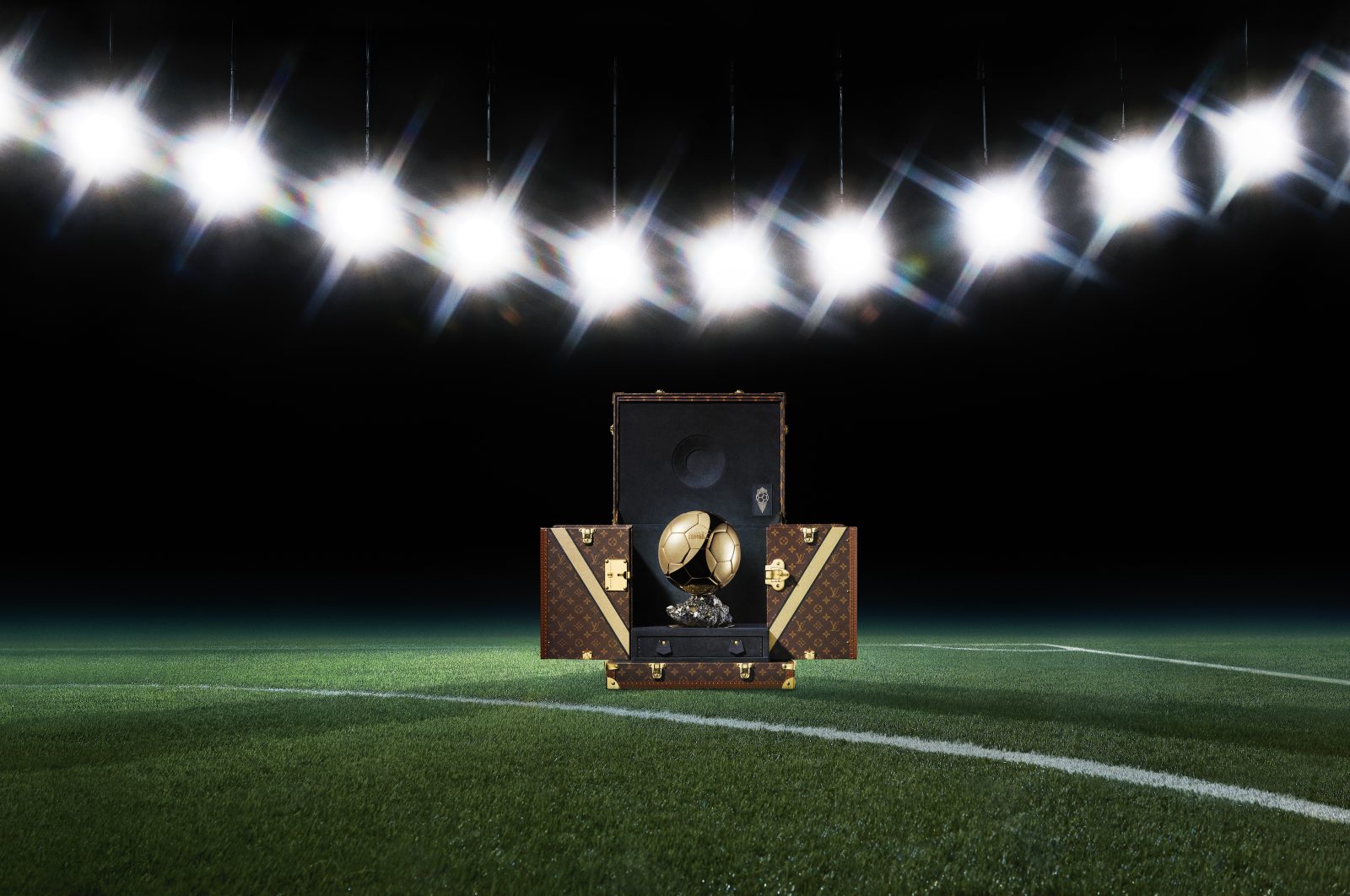 The Ballon d'Or trophy displayed in its bespoke Louis Vuitton Trophy Trunk on a football pitch, with the iconic Monogram canvas and gold "V" details visible. (Photo: Courtesy of Louis Vuitton)