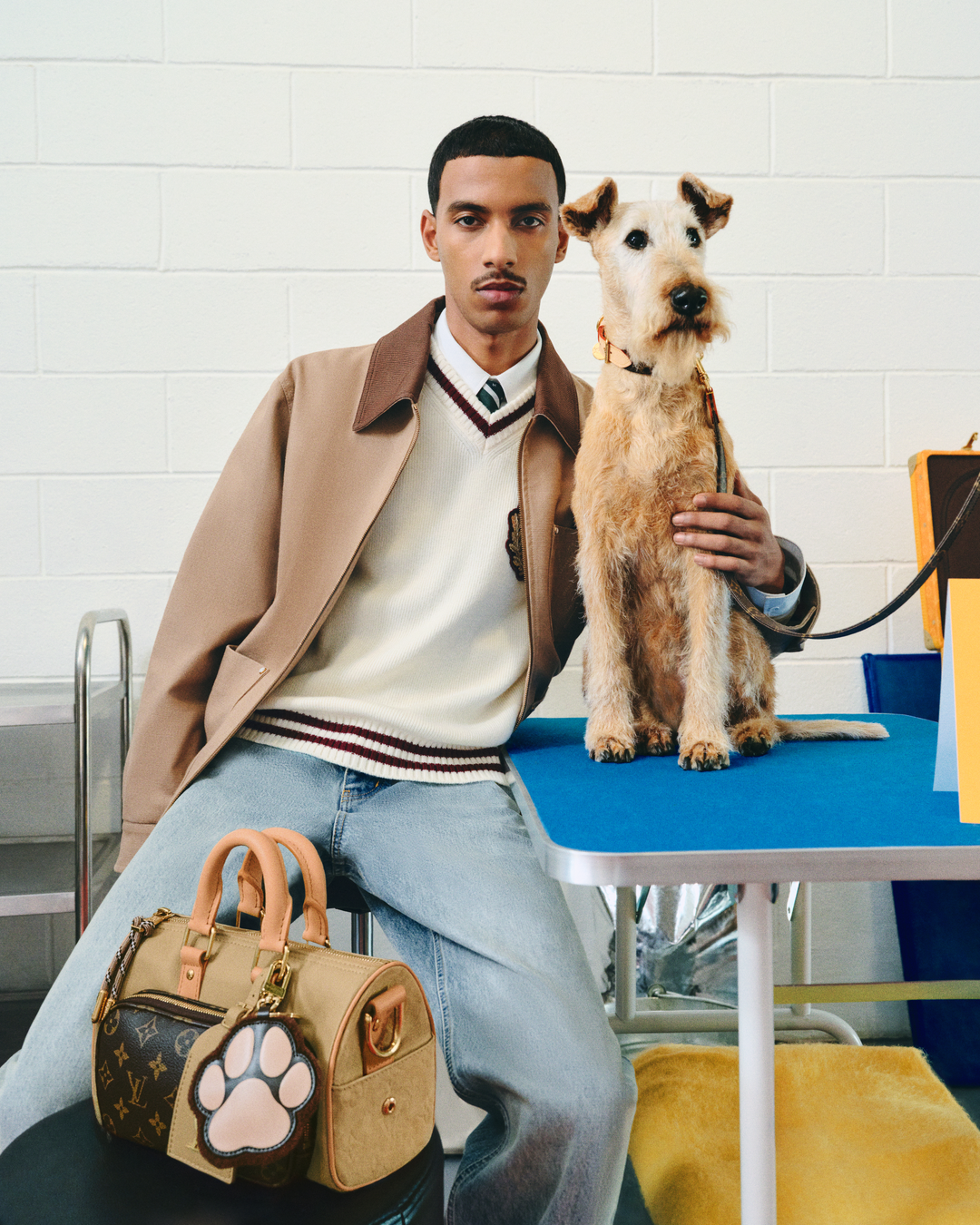 A Wire Fox Terrier companion showcases Louis Vuitton's new Dog LVππππ Pre-Collection, featuring a preppy cream V-neck sweater, camel coat, and Monogram canvas Speedy bag with paw print charm. (Photo: Courtesy of Louis Vuitton)