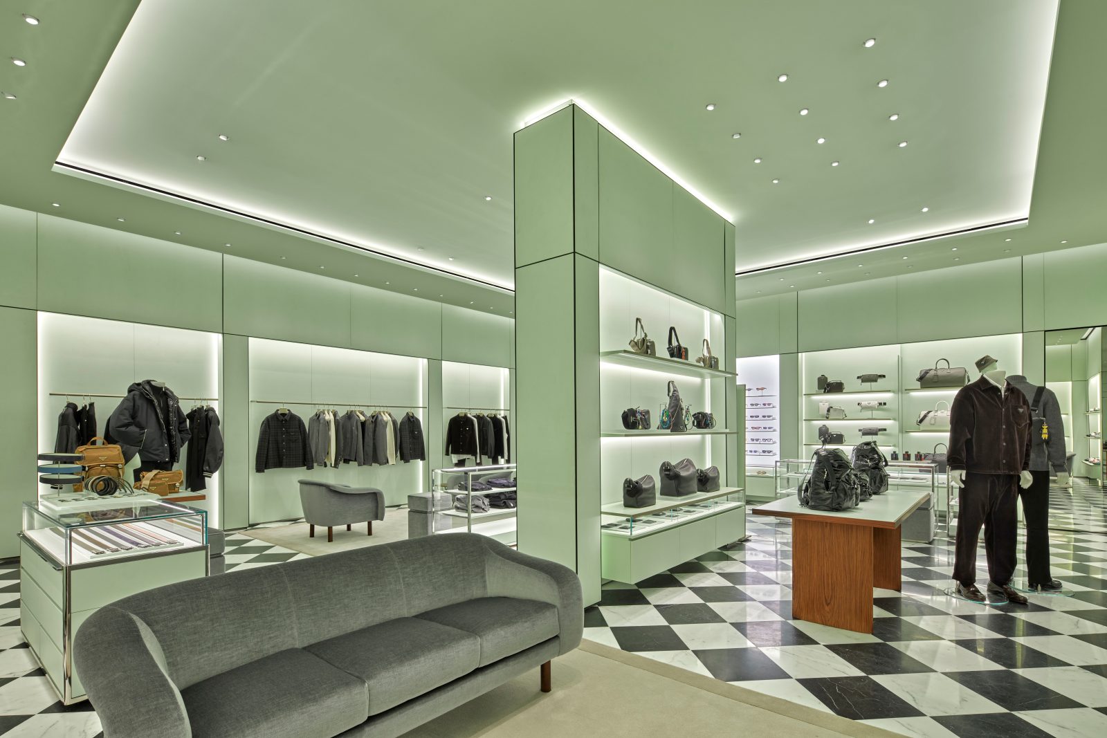 A view of the boutique's ready-to-wear and accessories assortment, where modern walnut display tables contrast with a Milanese-inspired geometric floor pattern. (Photo: Courtesy of Prada)