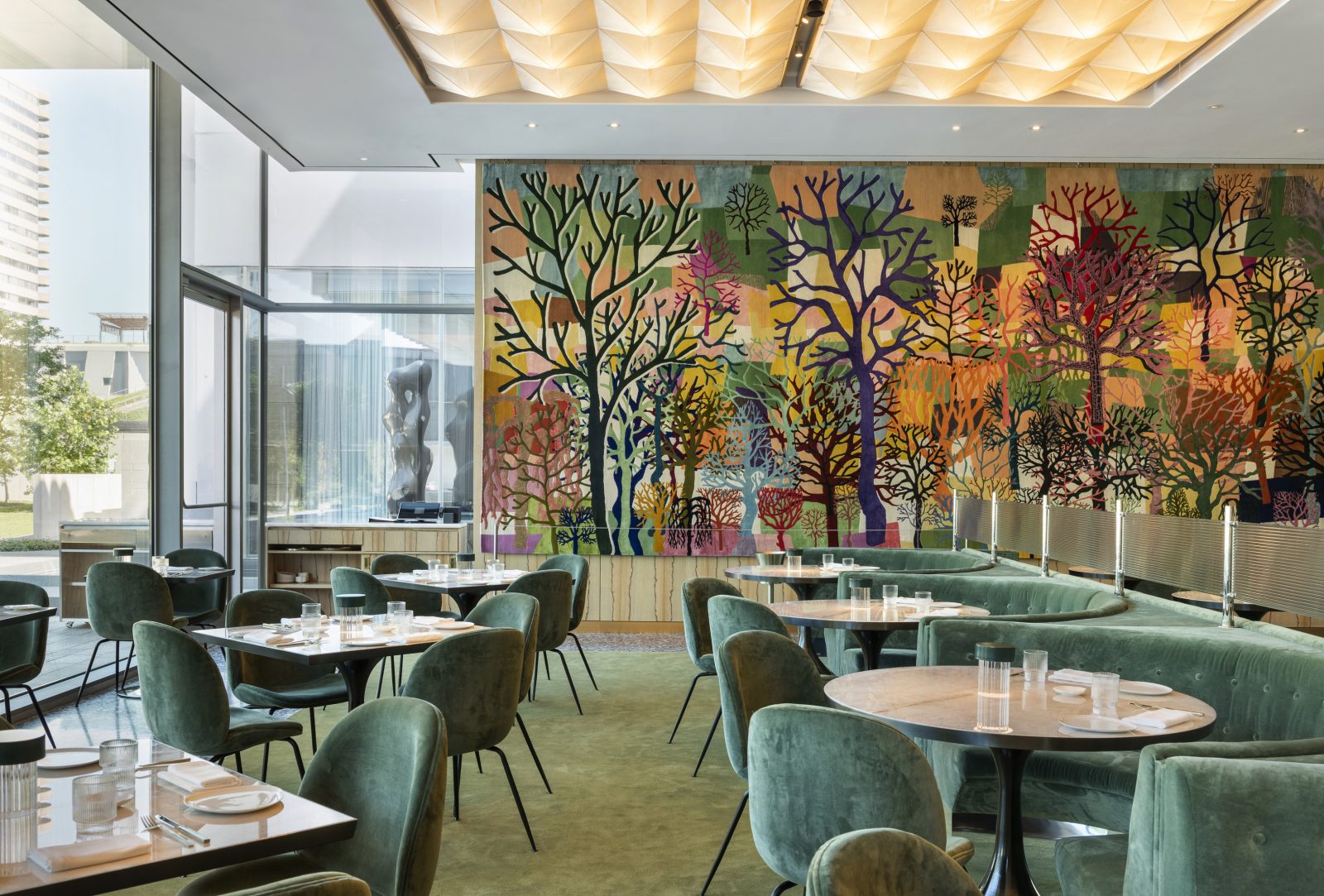 The dining room showcases Trenton Doyle Hancock's vibrant wall tapestry “Color Flash for Char and Chew, Paris Texas in Seventy-Two,” accentuated by sage velvet seating. A sculptural ceiling features Noguchi's Akari-inspired lighting. (Photo: Julie Soefer)