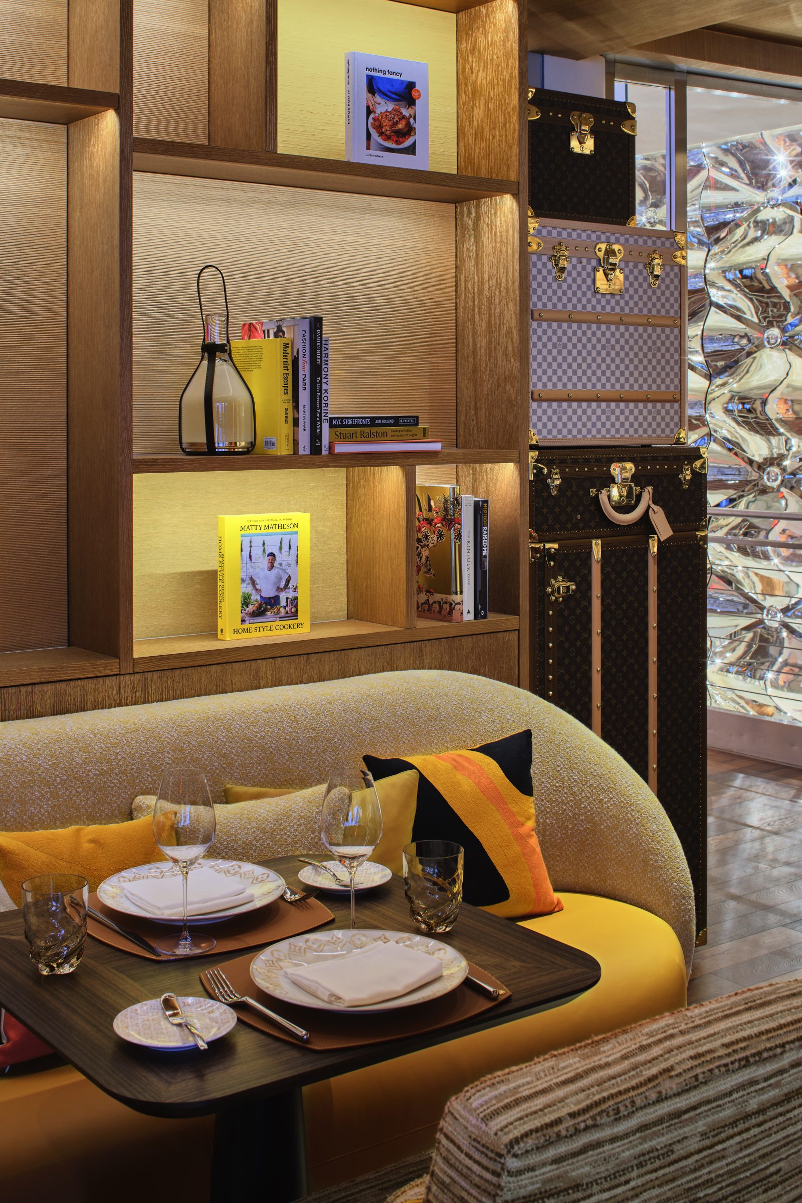 An intimate corner of Le Café Louis Vuitton’s library dining space, where curated culinary books and vintage trunks form a refined backdrop, complemented by custom tableware and warm amber accents.