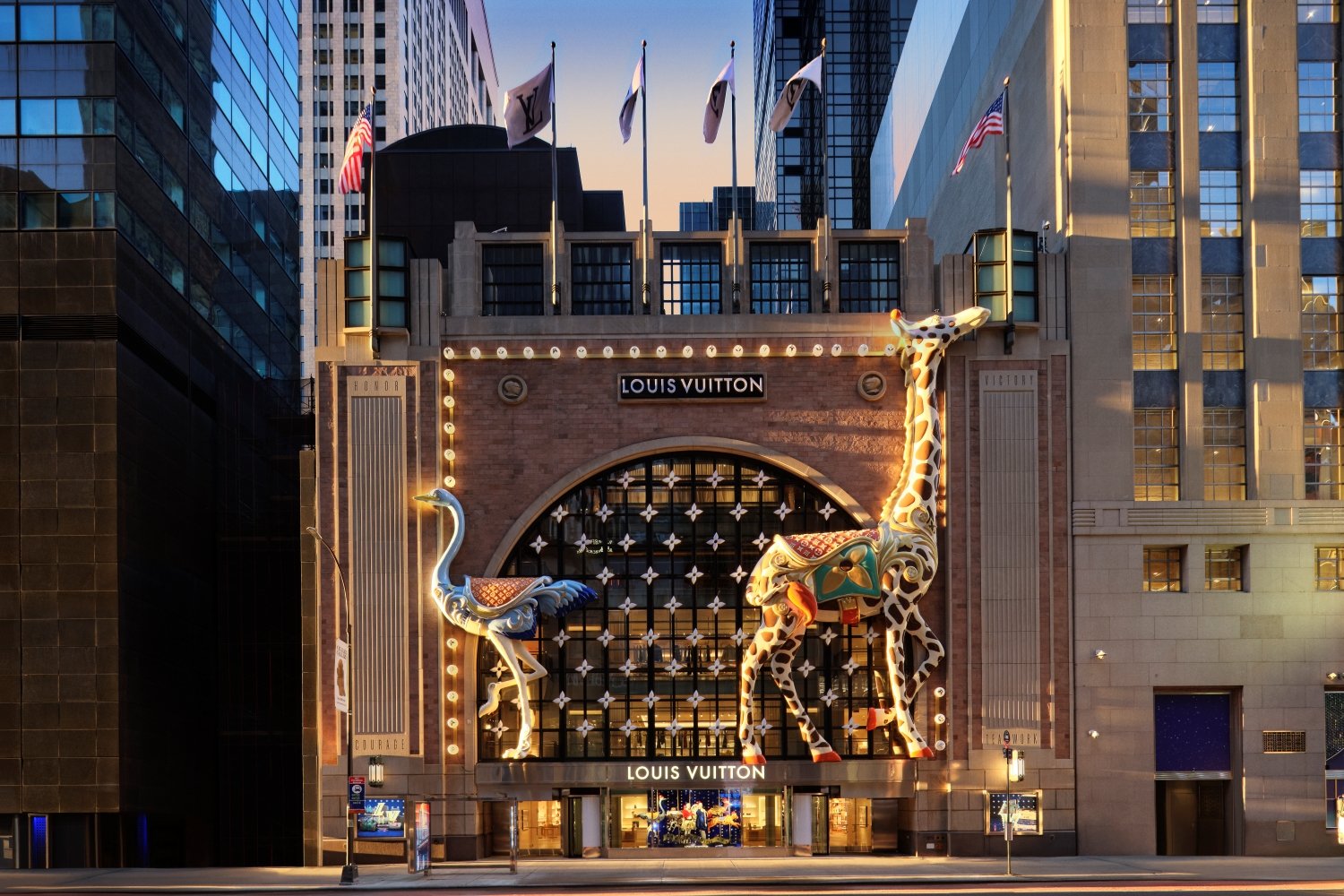 The temporary flagship’s Art Deco façade is brought to life with a whimsical carousel-themed holiday installation, featuring oversized illuminated giraffe and ostrich figures that frame the grand archway entrance.