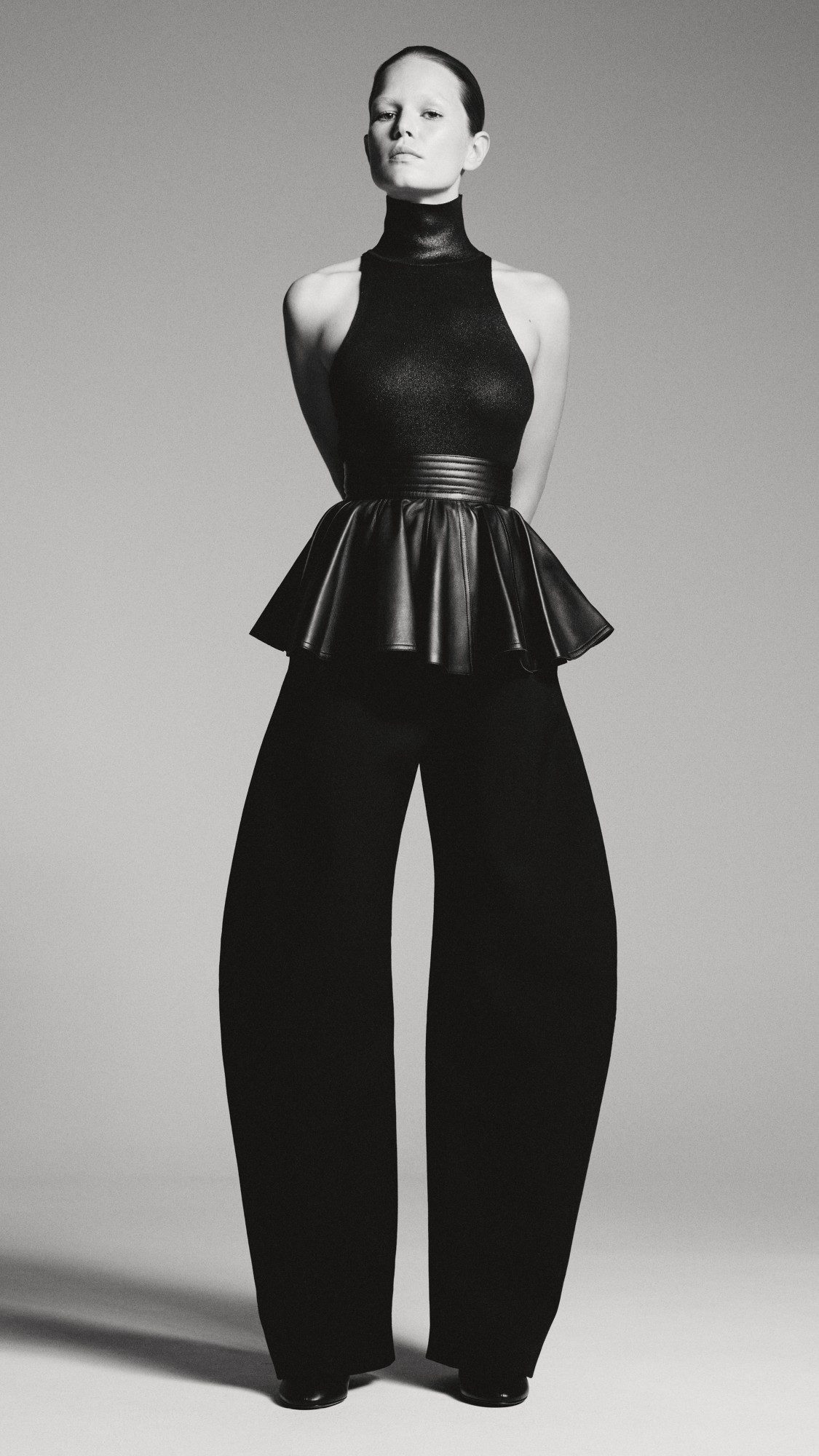 The ALAÏA silhouette is redefined with a modern twist, featuring a high-neck top and peplum belt that accentuates the brand’s signature craftsmanship.