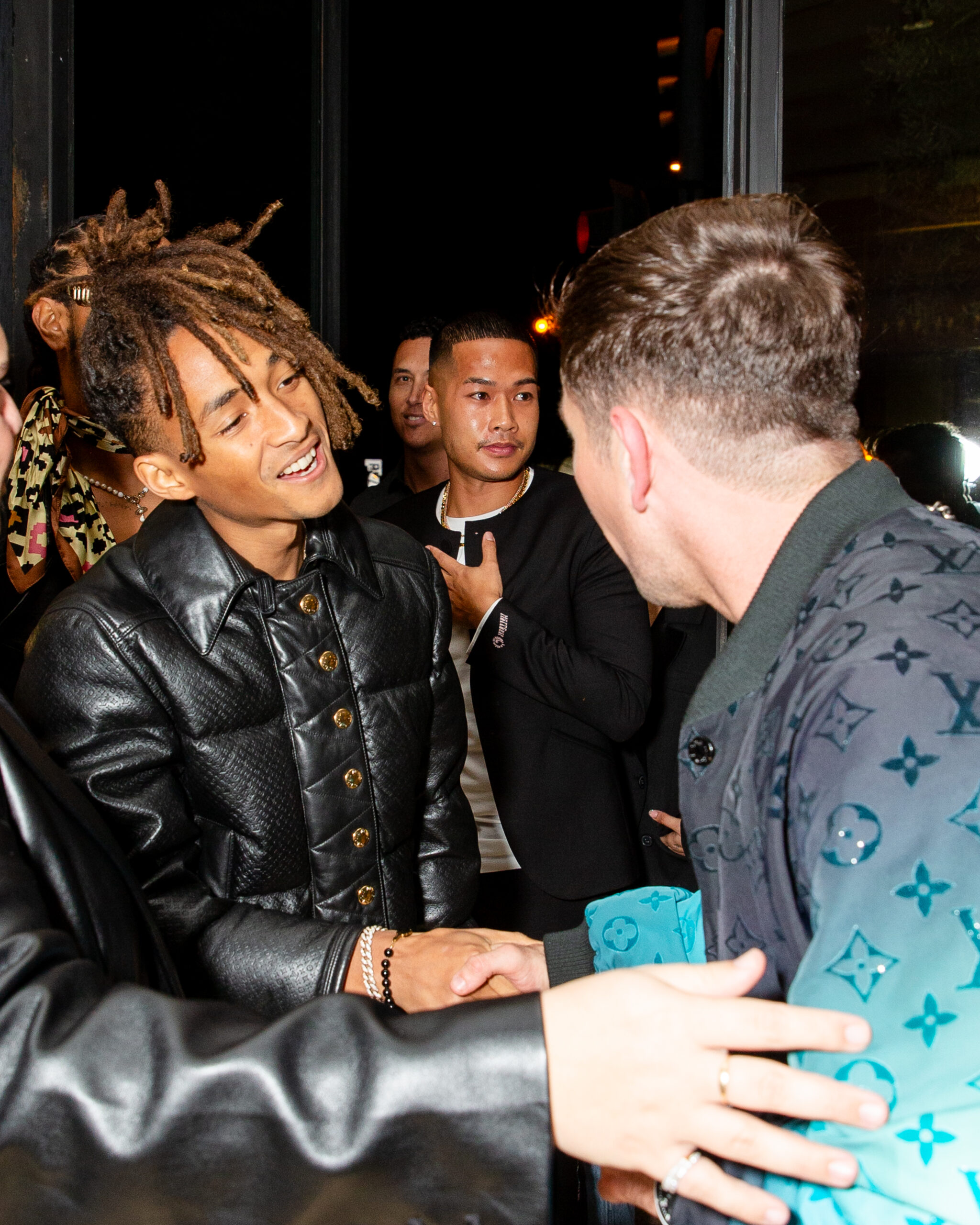 Jaden Smith, with his charismatic presence, greets Barry Keoghan at the Louis Vuitton SS24 pop-up party, donning a sleek leather jacket that mirrors the brand’s fusion of luxury and streetwear.