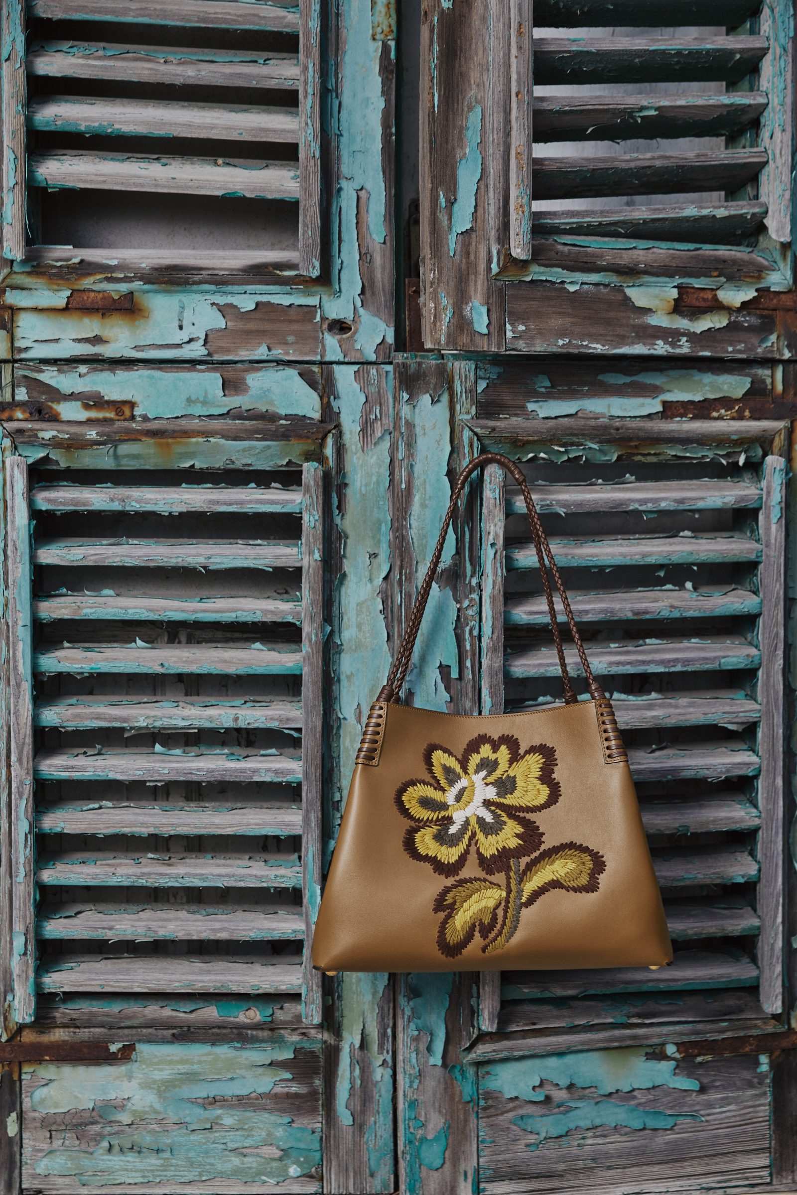 ETRO Libra Tote in walnut leather with embroidered flower motif against weathered turquoise shutters (Image: Courtesy of ETRO)