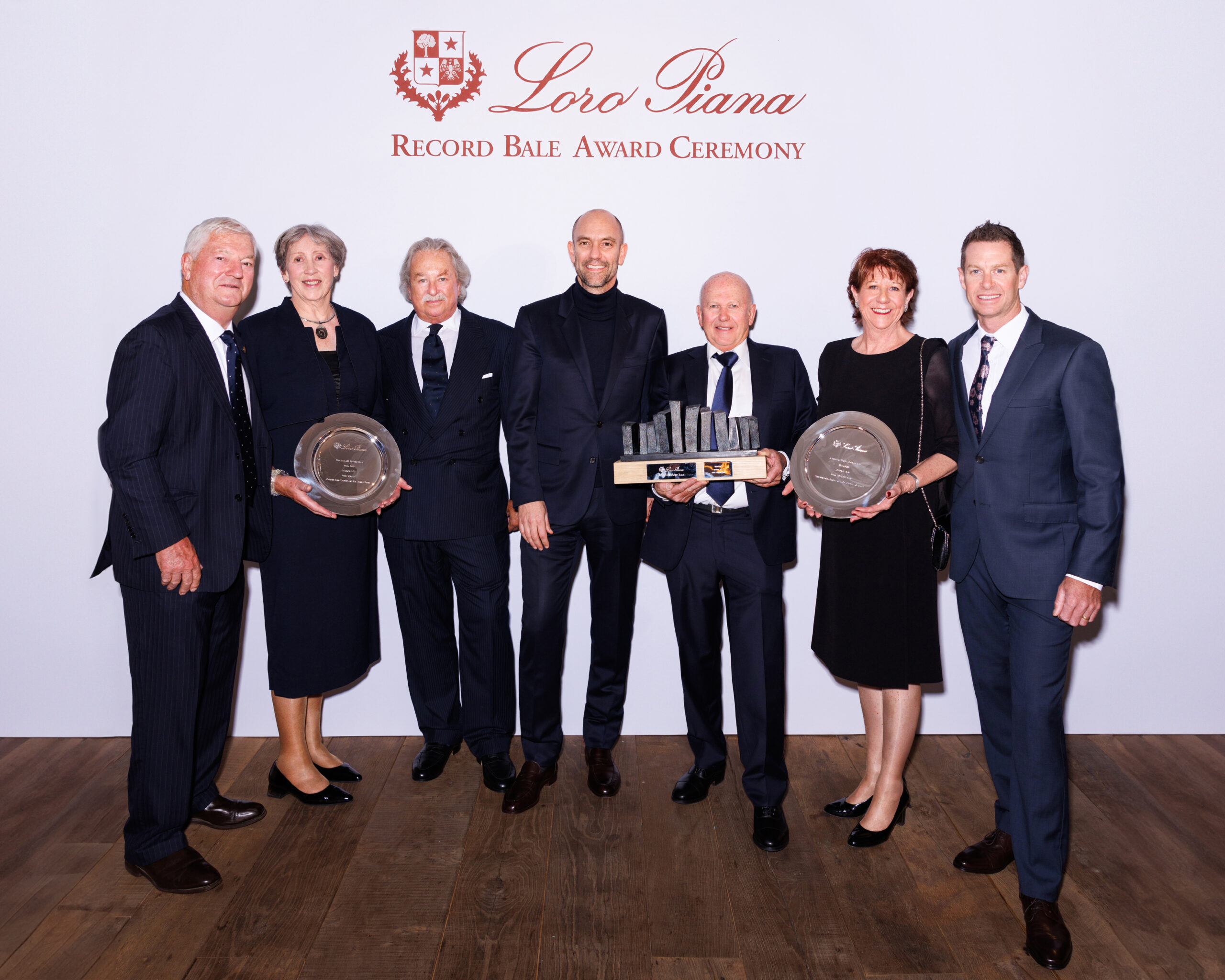 Award recipients stand proudly at the Loro Piana Record Bale Award Ceremony, a testament to exceptional craftsmanship and dedication. The awards they hold symbolize the pinnacle of achievement in the luxury wool industry.