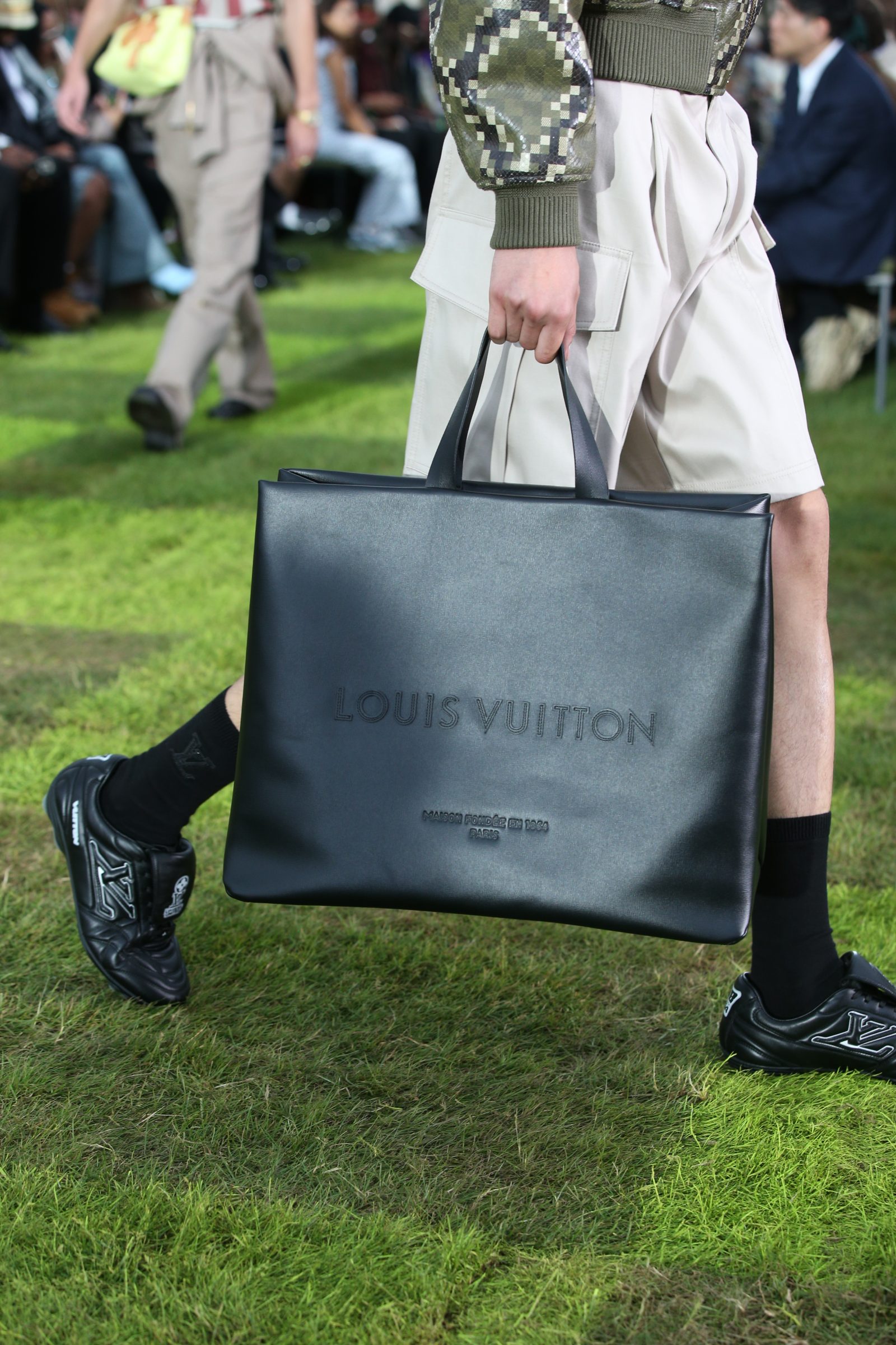 Sleek sophistication meets athletic edge: A structured noir leather tote pairs with the new LV Footprint Soccer shoe as seen on the Spring-Summer 2025 men's runway by Pharrell Williams. (Photo: Courtesy of Louis Vuitton)