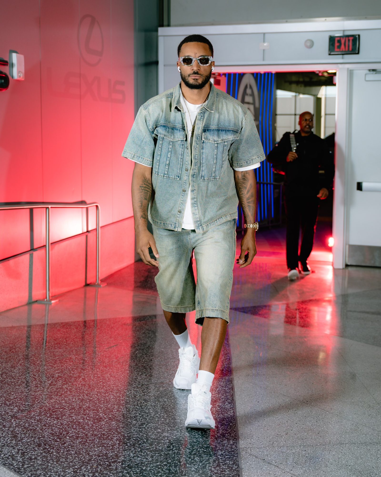 LA Clippers’ Norman Powell arrives in casual luxury, wearing a light-wash denim set from Versace, paired with white sneakers and sunglasses, highlighting the brand’s versatile sportswear aesthetic.