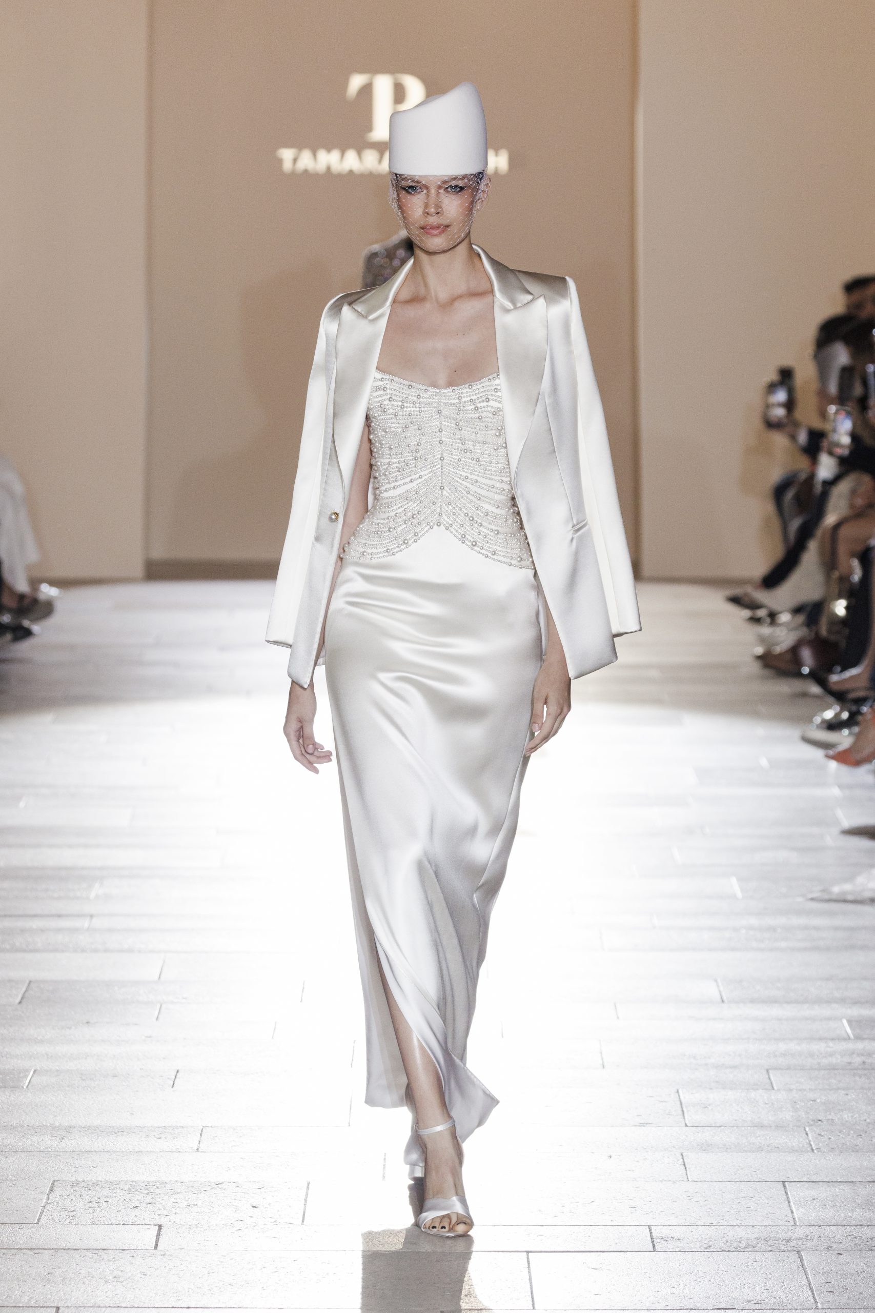 Look 6: White double satin gown featuring draped pearl corset detailing, accompanied by a white double satin tuxedo jacket and white felt crown