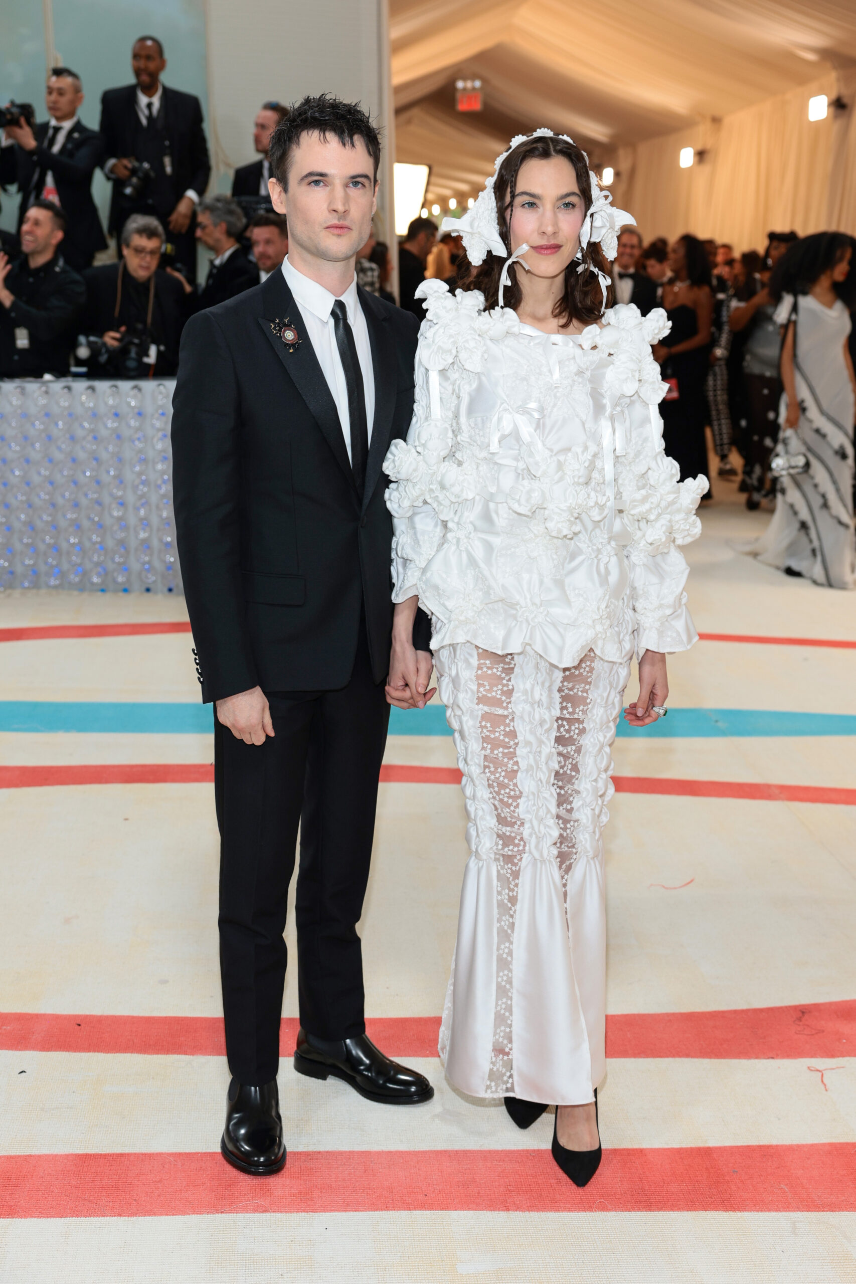Tom Sturridge and Alexa Chung wore a Dior men’s collection black wool peak lapel tuxedo, a white cotton classic collar shirt, a black silk tie, a black resin and gold-finish brass coral brooch and black leather chelsea boots